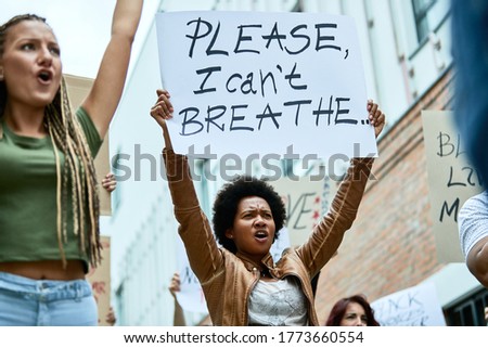 Low angle view of a black woman holding banner with I can't breathe inscription while demonstrating for human rights with crowd of people. 