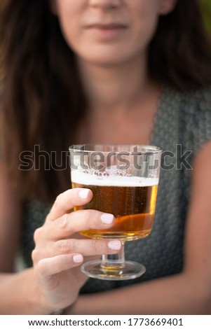 Beautiful brown woman in a green dress holding a glass of beer on a sunny terrace. Selective focus.