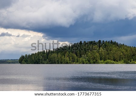 Beautiful summer landscape with a forest lake. View of the trees on the hilly shore of the lake. Cloudy weather before the rain.