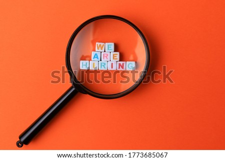 Text or inscription We are hiring. Cubes with letters under a magnifying glass on an orange background with copyspace. HR concept.