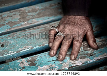rings of an old man’s hand in a blue wooden chair