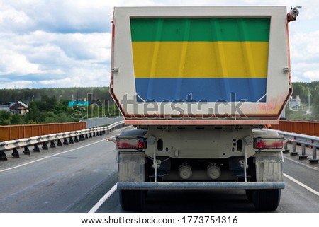 Big  truck with the national flag of  Gabon moving on the highway, against the background of the village and forest landscape. Concept of export-import,transportation, national delivery of goods 
