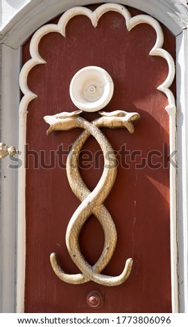 A fragment of a wooden door with the image of two snakes in an arched opening, on a burgundy background.