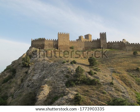 Scenic view of the Fortress mountain, covered with shrubs and faded grass in the sun and an ancient fortress with a defensive wall and towers on a warm summer evening. Genoese fortress, Sudak, Crimea Royalty-Free Stock Photo #1773903335