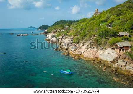 Tropical island coastline, Coast of Koh Tao island with turquoise clear water, boat and people snorkeling, bungalows with sea view, sunny day. Famous destination for travel holidays in Thailand