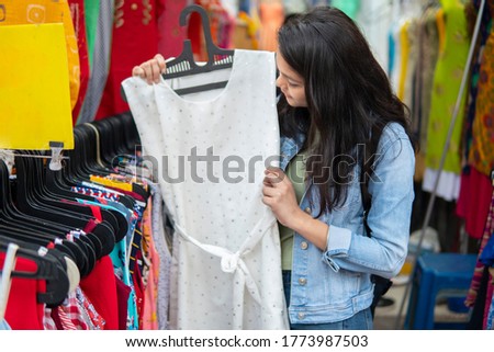 Happy late teen girl looking and buying clothes from outdoor street market of Delhi, India at day time. shoot location Sarojini Nagar, Delhi, India.
 Royalty-Free Stock Photo #1773987503
