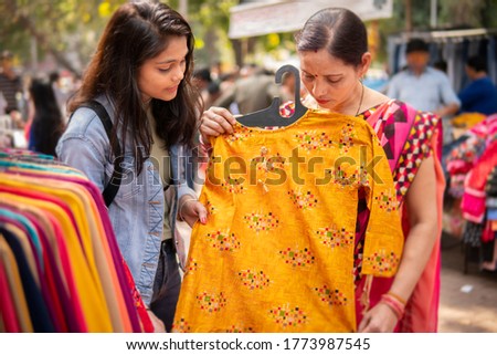 Happy mother and daughter looking and buying clothes together from outdoor street market of Delhi, India at day time. shoot location Sarojini  Nagar, Delhi, India.
 Royalty-Free Stock Photo #1773987545