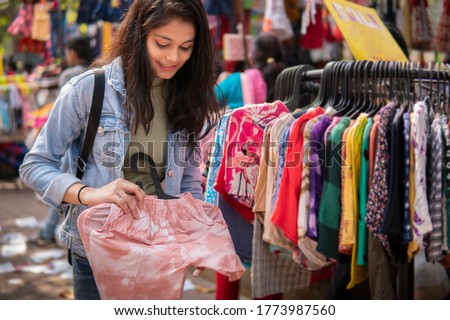 Happy late teen girl looking and buying clothes from outdoor street market of Delhi, India at day time. shoot location Sarojini Nagar, Delhi, India.
 Royalty-Free Stock Photo #1773987560