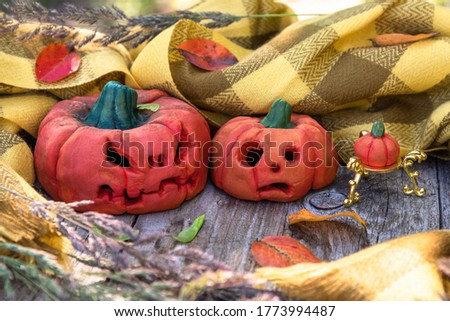 Halloween-style pumpkins on a background of a checkered yellow scarf and fallen autumn leaves.