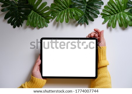 Woman using a mobile phone, blank screen on a white desk with green leaves