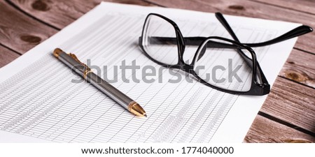 On a dark wooden table lies a document with a pen and glasses. Top view close up. Business concept
