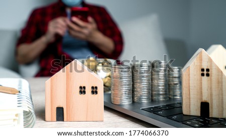 Wood house model on the table with blurred businessman using smartphone background. Working for financial gold and profit concept