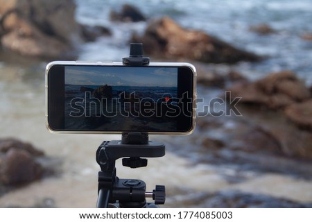 Close-up Smartphone take a sea on the beach with large rocks seascape photo and video time lapse on stand Mobile tripod