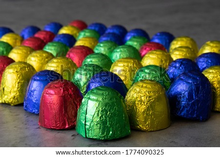 Chocolate bonbons in multicolored wrapping foil on dark background. Colorful sweets with focus on foreground with gradual blur into the background