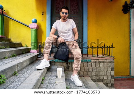 Urban style. Fashion portrait of a stylish young man with sunglasses posing on a street by old building with yellow wall. Male fashion. Colorful background.