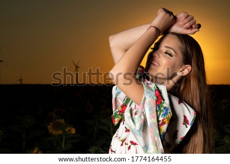 Beautiful young girl posing in a sunflower field at sunset 