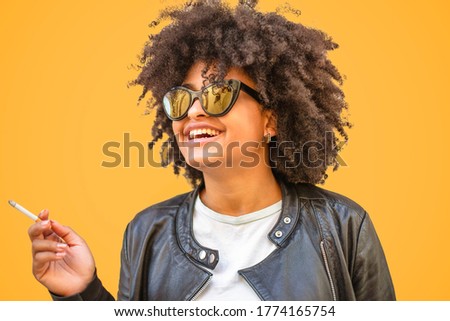Smiling young African-American woman holds a cigarette on a orange background.