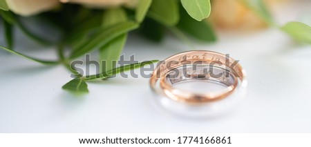 Two wedding rings in yellow and white gold, engraved with the Latin words "so fated" on the background of a wedding bouquet of roses. Wedding concept, romantic greeting card. Banner Royalty-Free Stock Photo #1774166861