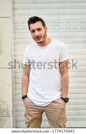 Men's street youth modern fashion. A young male hipste posing against a white roller shutter blinds. White T-shirt

           