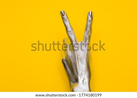 Elegant female hand with a silver paint on it shows two fingers, isolated on a yellow background. Free space for text