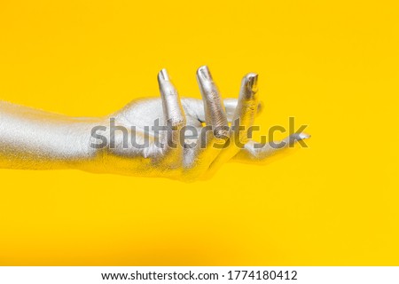 Elegant female hand with a silver paint on it, isolated on a yellow background. Free space for text