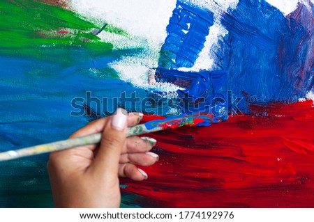 Female artist works on abstract painting, moving paint brush energetically she creates modern masterpiece. Creative studio where large canvas stands on easel Illuminated. Low Angle