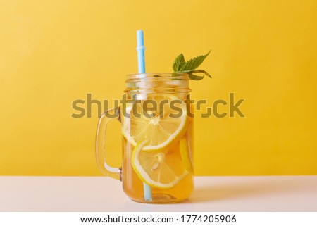 Close up shot of fresh drink with lemons and mint, glass jug filled with cocktail and lemon slices and drinking tube, cold summer refreshing lemonade.