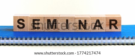 SEMINAR word written on wooden blocks with black letters, a row of blocks is located on a blue notepad