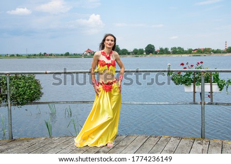 
Beautiful young girl with red lips in a long yellow dress. She stands on a bridge near the lake.