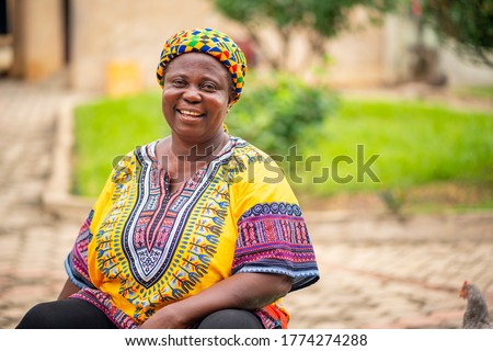 image of black mother with beautiful African print dress and head wrapper-African woman smiling in her garden-black woman sitting on a chair with joy and happiness.