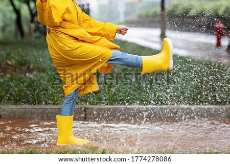 Cute little girl in yellow raincoat and rubber boots walking outdoor during rain. Bad weather, summer tropical storm, autumn fashion concept. Royalty-Free Stock Photo #1774278086