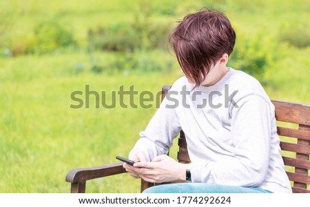 A girl in home clothes sitting on a bench with a smartphone in her hand