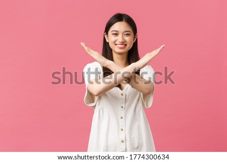 Beauty, people emotions and summer leisure concept. Cheerful smiling asian girl asking politely to stop, show cross sign in prohibition and forbid, smiling happy, standing pink background