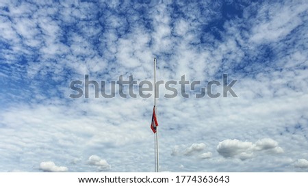 The national flag was dropped in half. The background is bright, with beautiful streaks and clouds.Reduce the flag at half mast to mourn the important person who died.