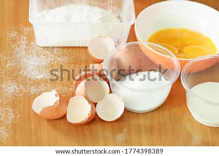 Picture of a ingredien of cook bread, eggs with flour, sugar, oil, egg yolks and used eggshells, with powdered flour sprinkled on the floor, there is copy space for text.