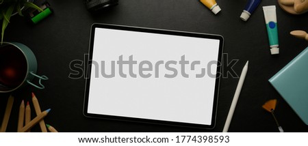 Top view of mock up digital tablet and stylus on black table with painting tools, notebook and cup  