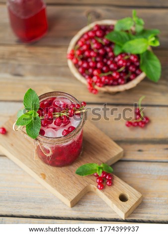 Glass of red currant cocktail or mocktail, refreshing summer drink with crushed ice and sparkling water on wooden background.