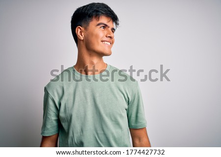 Young handsome man wearing casual t-shirt standing over isolated white background looking away to side with smile on face, natural expression. Laughing confident.