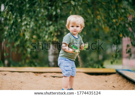 Picture of pretty little boy in light T-shirt and shorts plays in a sandbox with plastic toys in the summer vacations.