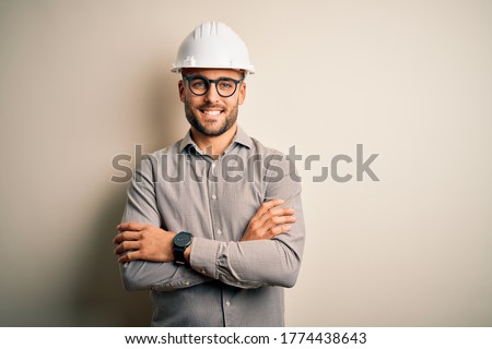 Young architect man wearing builder safety helmet over isolated background happy face smiling with crossed arms looking at the camera. Positive person. Royalty-Free Stock Photo #1774438643