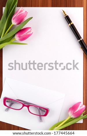 Blank card, pen, glasses and tulips on a wooden background