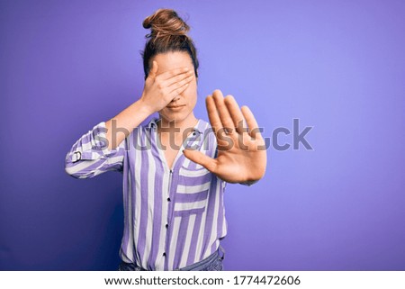 Young beautiful blonde woman wearing casual striped shirt standing over purple background covering eyes with hands and doing stop gesture with sad and fear expression. Embarrassed and negative concept