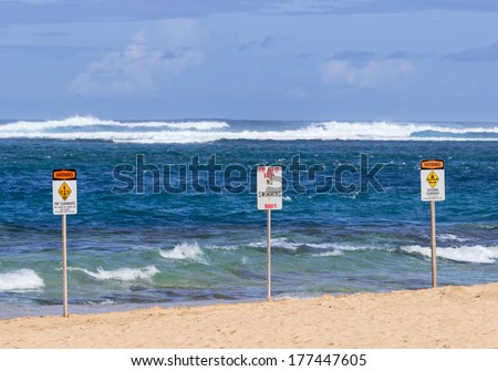Three warning sign no swimming and strong currents in treacherous winter waters on Tunnels Beach in Kauai Hawaii