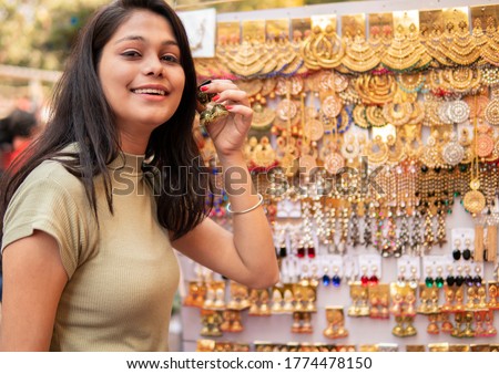 Happy girl shopping for earrings from outdoor street market and looking at camera with toothy smile. Shoot location Sarojini Nagar, Delhi, India.
 Royalty-Free Stock Photo #1774478150