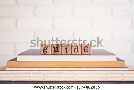 The word GUIDE, alphabets on wooden rubber stamps on top of books with bricks background, blank copy space, vintage minimal style. Concepts of instruction, learning, manual, policy, and education. Royalty-Free Stock Photo #1774482836