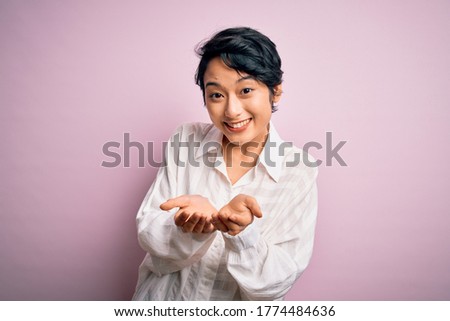 Young beautiful asian girl wearing casual shirt standing over isolated pink background Smiling with hands palms together receiving or giving gesture. Hold and protection