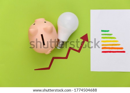 The concept of energy and money saving. Energy class, growth arrow tending up with light bulb and pigy bank on green background. Top view