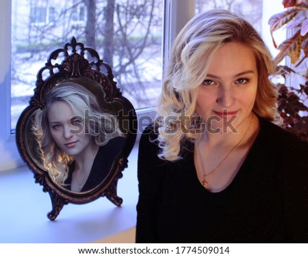 Portrait of a beautiful girl with a reflection of her second dark personality in a vintage mirror on the background of a window