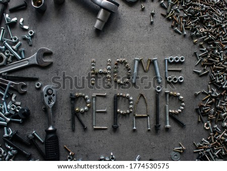 Home repair sign made of old nuts and bolts. Wrench tool, old nuts and bolts of different sizes top view photo. Grey textured concrete background with copy space. Handyman tools close up picture. 