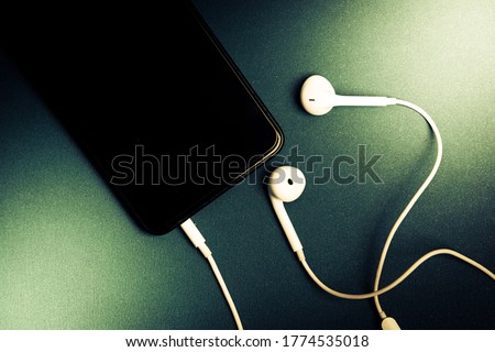 white headphones plug in smart phone , Isolated on a shiny black background , Drak green